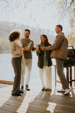 Four friends gather on a wooden deck at sunset, sharing laughter and drinks while enjoying nature's beauty.の写真素材
