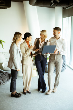 Four colleagues engage in a discussion, sharing ideas and showcasing a laptop in a stylish office space filled with greenery.の写真素材