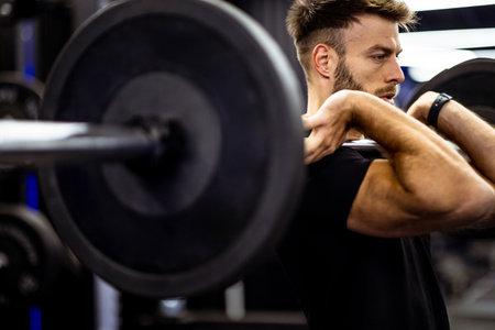 A man performs a weightlifting exercise in a modern gym. He focuses intently while lifting a...