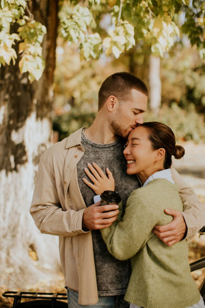 A woman and a man embrace in a park, enjoying each other's company amidst colorful autumn leaves.の写真素材