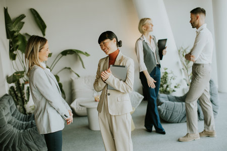 Five business professionals interact in a bright, modern office space. They share ideas while standing amid stylish furniture and plants, fostering collaboration and teamwork.の写真素材