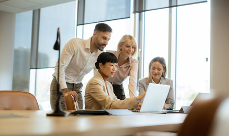 Four professionals gather around a laptop in a bright office. They discuss ideas and share insights, working together to solve problems and innovate. The atmosphere is focused and collaborative.の写真素材