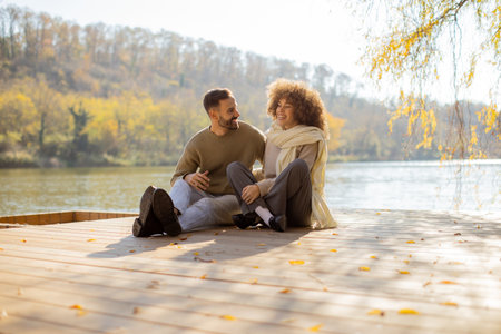 A couple shares joyful moments on a wooden dock, surrounded by autumn foliage and a tranquil lake.の写真素材