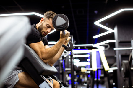 A man works hard at a gym, focusing on his bicep curls. The modern space features bright, colorful...