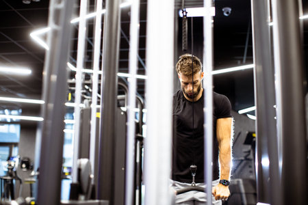 Man  focuses on his workout at a modern gym, utilizing cable machines to enhance his upper body...
