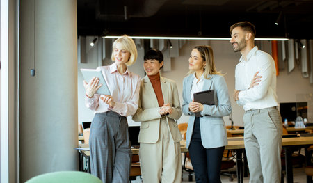 Four professionals gather in a contemporary office to discuss a project. They are engaged with a tablet, sharing ideas and collaborating. The environment is lively and conducive to teamwork.の写真素材