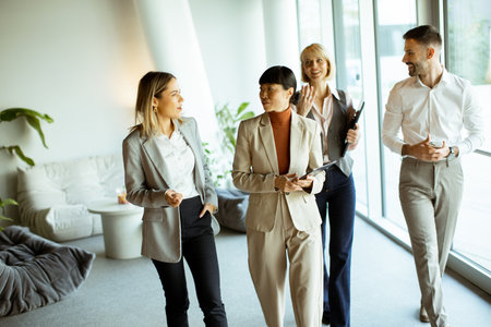 Four business professionals are engaged in conversation in a bright, contemporary office. They appear to be sharing ideas, showcasing collaboration and teamwork.の写真素材
