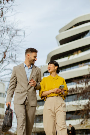 Two business professionals stroll and converse outdoors near a modern architectural structure. They share smiles and appear engaged in their discussion during daytime.の写真素材