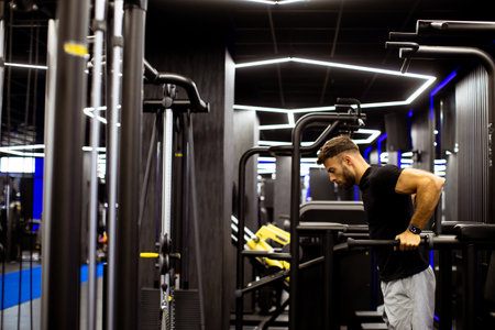 A man performs strength training using workout machines in a sleek, contemporary gym. The space...