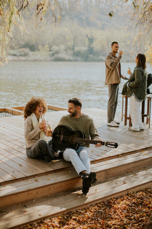 A group of friends relax by a serene lake, sharing drinks, music, and laughter on a sunny afternoon.
