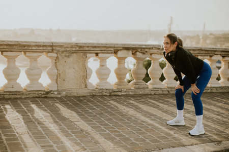 A woman is taking a break after exercising in Malta. She is in an outdoor area with a historic wall...