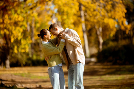 A Korean woman and a Caucasian man laugh and dance together in a vibrant autumn park filled with...