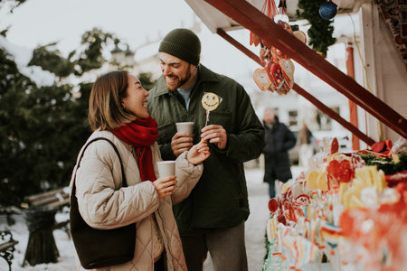 A Korean woman and Caucasian man stand at a candy stall at a Christmas market. The happy couple is...