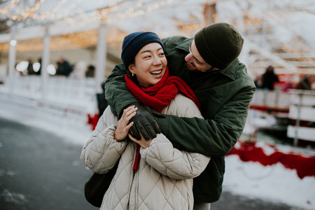 A Korean woman and a Caucasian man stand close in a winter setting filled with snow. They share smiles and warmth while enjoying the festive atmosphere around them.の写真素材