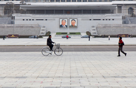 Pyongyang, North Korea - November 10, 2016: Cyclist rides through Kim Il Sung Square near large...