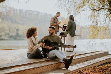Friends gather by the serene lake on a sunny autumn day, sharing drinks and music while enjoying each other's company.の写真素材