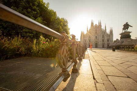 A young woman walks with grace by the stunning Duomo cathedral in Milan, basking in the golden sunlight of the afternoon.の写真素材