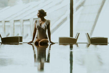 A woman sits near the water in a modern space. The sunlight enters through large windows. She looks...