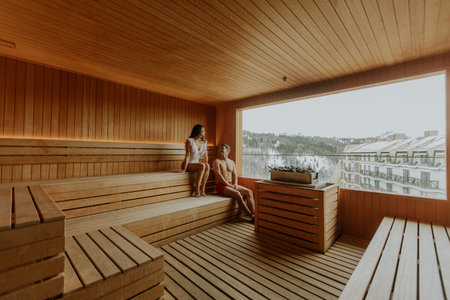 Two friends enjoy a peaceful moment in a wooden sauna, overlooking nature's beauty on a quiet...