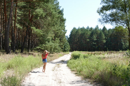 a young girl in blue shorts and a pink t-shirt walks barefoot along the sandy road near the forestの写真素材