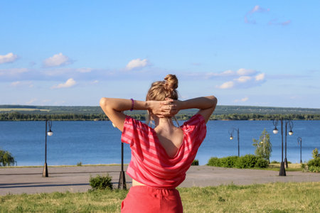 a young girl student in a t-shirt stands on the embankment by the river on vacation in natureの写真素材