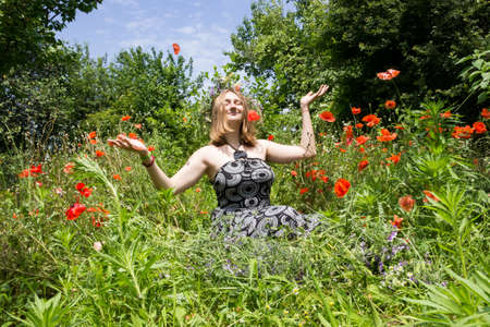 young girl student in a wreath of wild grasses sits on a field with blooming red poppies on vacation in natureの写真素材