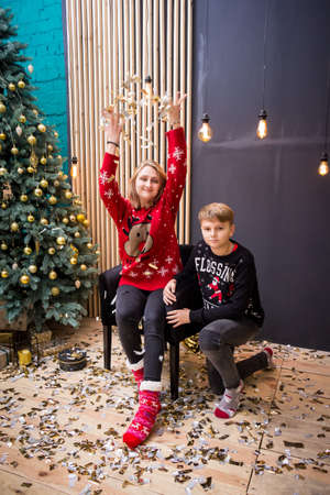 young blonde girl sitting in a chair in a red wreath and in a red New Year's sweater with a boyの写真素材