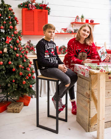 young blonde girl sitting on a high chair in a red christmas sweater with a boy in the christmas kitchenの写真素材