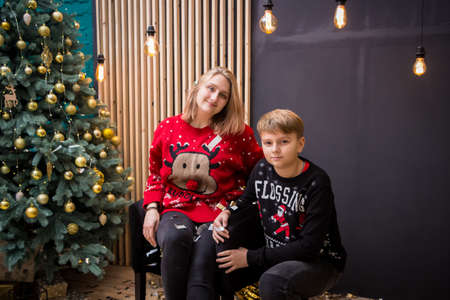 young blonde girl sitting in a chair in a red wreath and in a red New Year's sweater with a boyの写真素材