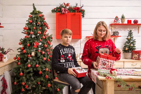 young blonde girl in a red christmas sweater with a boy sitting on a high chair in the christmas kitchenの写真素材