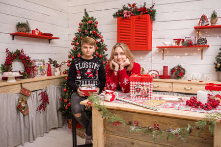 young blonde girl in a red christmas sweater with a boy sitting on a high chair in the christmas kitchenの写真素材