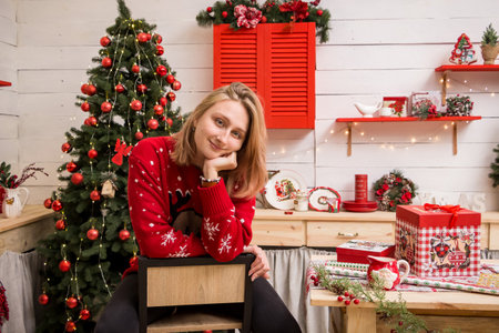 young blonde girl sitting on a high chair in a red christmas sweater in the christmas kitchenの写真素材