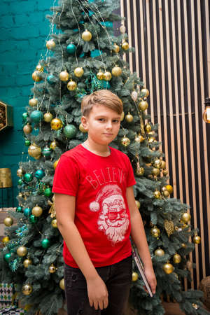 a boy in a red New Year's T-shirt standing by a decorated Christmas tree in New Year's decorationsの写真素材