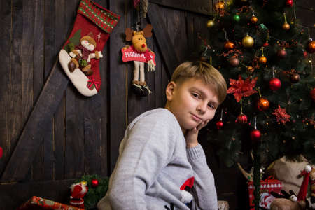 handsome boy in a New Year's sweater at a decorated Christmas tree in New Year's decorationsの写真素材
