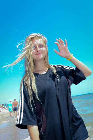 young girl schoolgirl in a big black T-shirt on the azure seashore on a sandy beachの写真素材