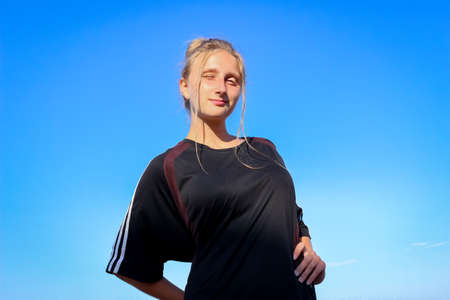 young girl schoolgirl in a big black T-shirt on the azure seashore on a sandy beachの写真素材