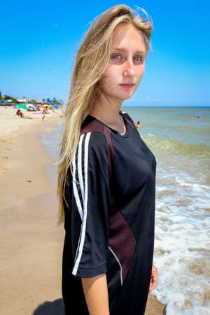 young girl schoolgirl in a big black T-shirt on the azure seashore on a sandy beachの写真素材