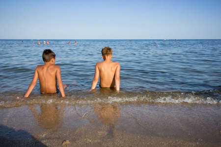 Two boys sitting in the sea water and looking at each other.の写真素材