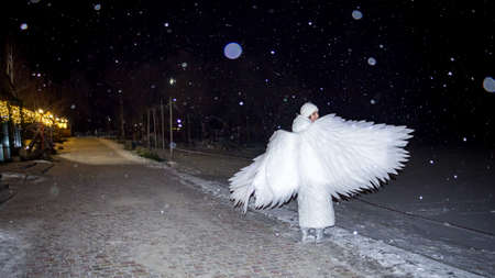 white angel girl under flying snow at night on the lake in winterの写真素材