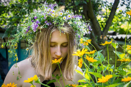 girl in a sundress and a wreath of wild flowers in the garden near yellow daisiesの写真素材
