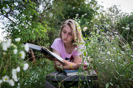 a young girl reads a book lying in the grass in an old garden in summerの写真素材