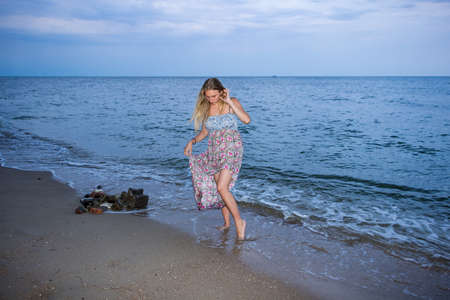 a young girl in the evening on the seashore in a sundress and with a hat, sunset, blue sky, clouds, calm, surf, sand, empty beach, wildの写真素材