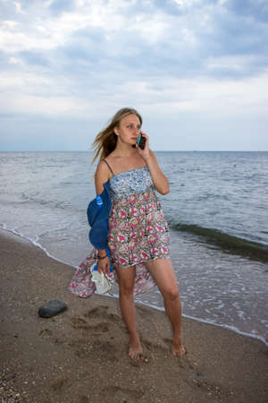 a young girl in the evening on the seashore in a sundress and with a hat, sunset, blue sky, clouds, calm, surf, sand, empty beach, wildの写真素材