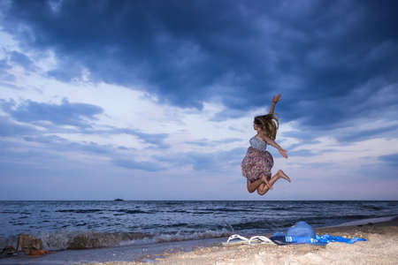 a young girl in the evening on the seashore in a sundress and with a hat, sunset, blue sky, clouds, calm, surf, sand, empty beach, wildの写真素材