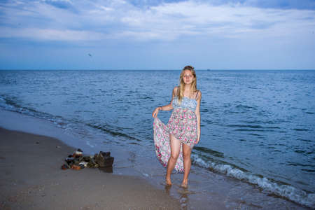 a young girl in the evening on the seashore in a sundress and with a hat, sunset, blue sky, clouds, calm, surf, sand, empty beach, wildの写真素材