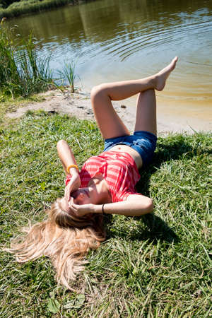 a girl lies on the shore of a forest lake, looks into the frameの写真素材