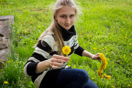 a young girl in a striped sweater weaves a wreath of yellow dandelionsの写真素材