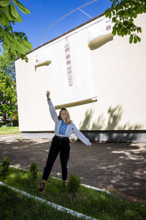 a young girl in a traditional Ukrainian embroidered shirt stands near a huge embroidered shirt on the buildingの写真素材