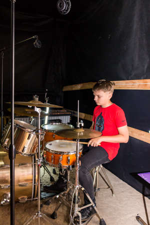 a young drummer plays drums, cymbals with sticks, sitting on a special chairの写真素材