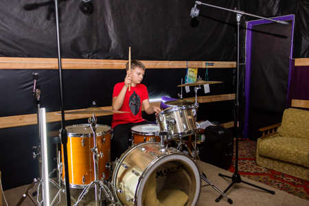a young drummer plays drums, cymbals with sticks, sitting on a special chairの写真素材
